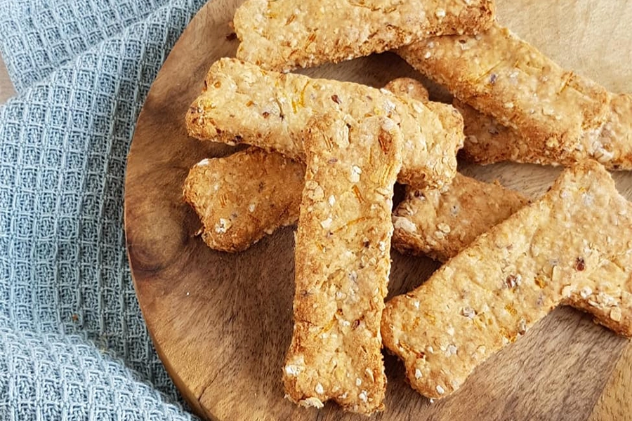 Biscuits pour chien faits maison, en forme d'os, à base d'avoine et d'autres ingrédients naturels, disposés sur une planche en bois