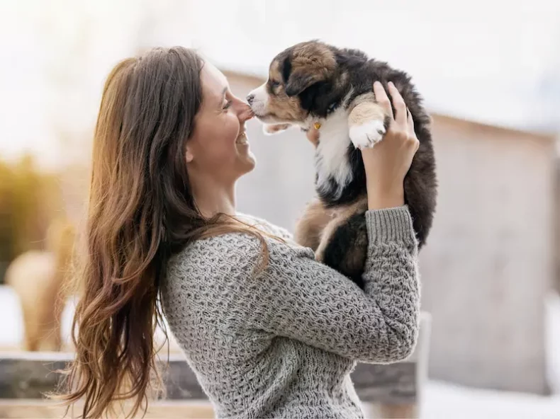 Une femme souriante tenant un chiot dans ses bras, illustrant l'amour et le lien entre les humains et leurs chiens.