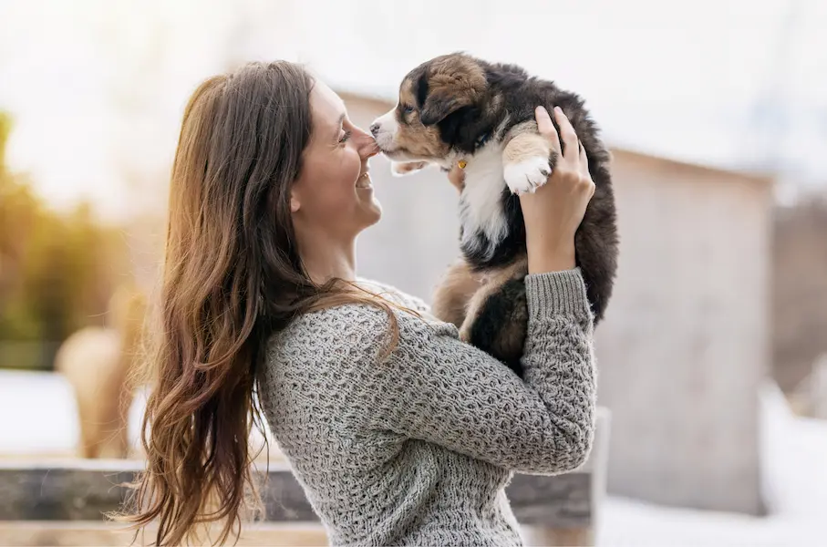 Une femme souriante tenant un chiot dans ses bras, illustrant l'amour et le lien entre les humains et leurs chiens.